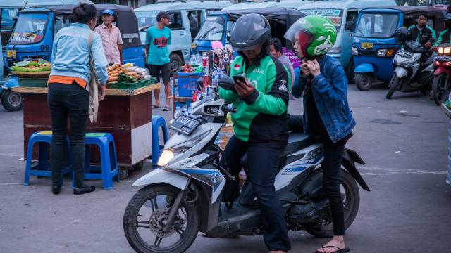 A passenger on a motorcycle rider fixes her helmet.